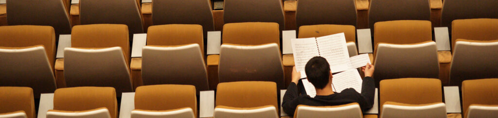 A student sits in an empty auditorium filling out papers.