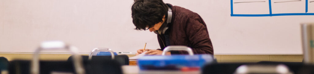 A male university student leans over his desk filling out an assessment.