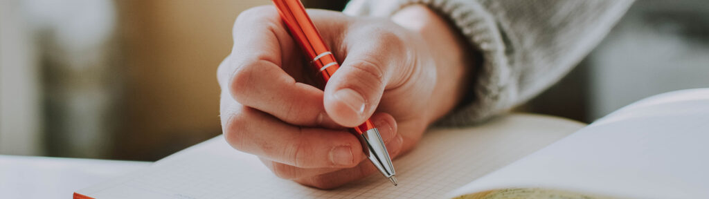 A learner holding a pen is prepared to begin writing a journal entry.